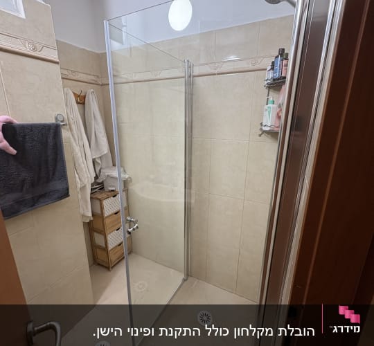 מקלחת עם דלת זכוכית ומדף עם מוצרי רחצה